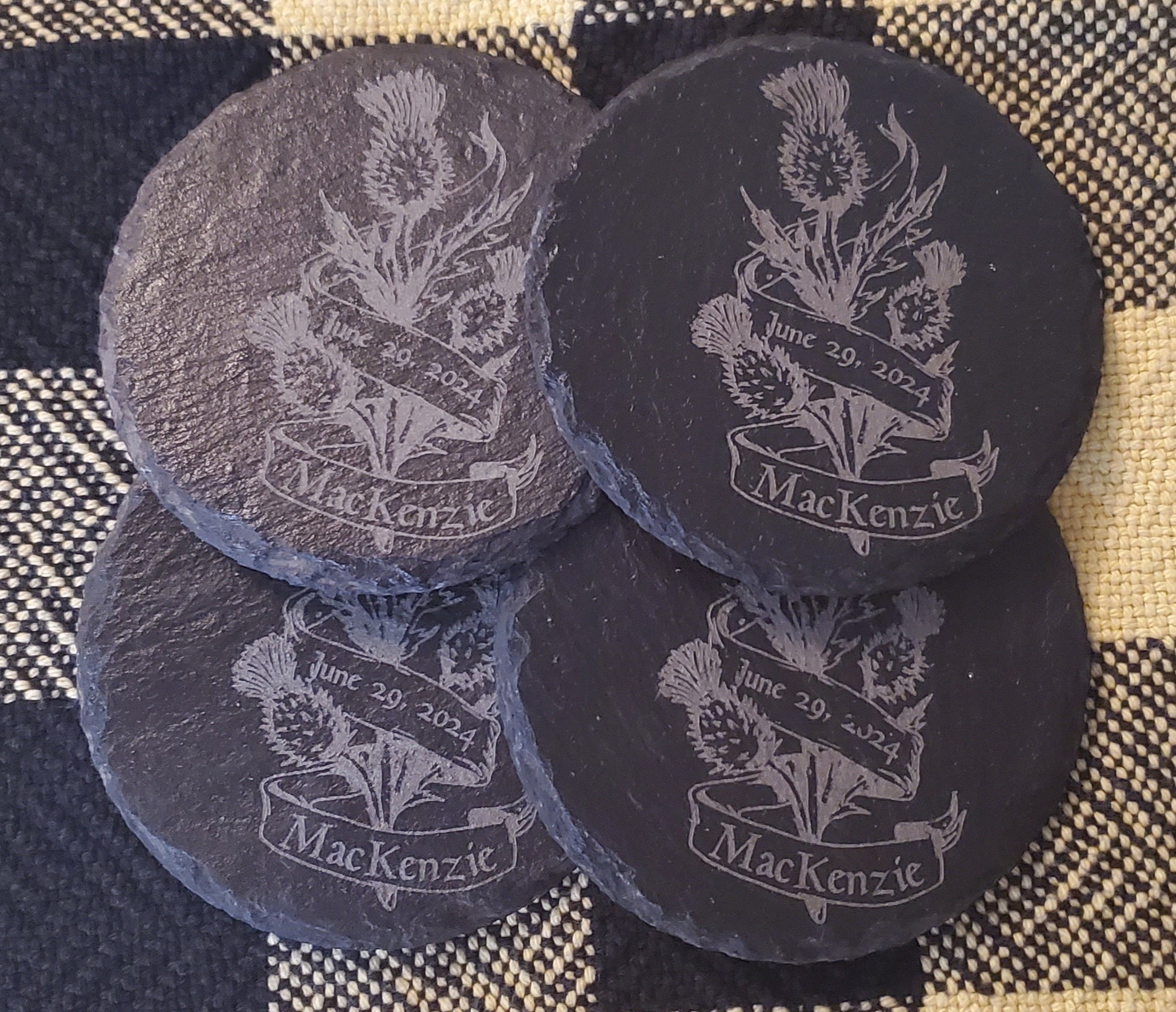 Four black slate coasters with engraved thistle design and 'MacKenzie' text