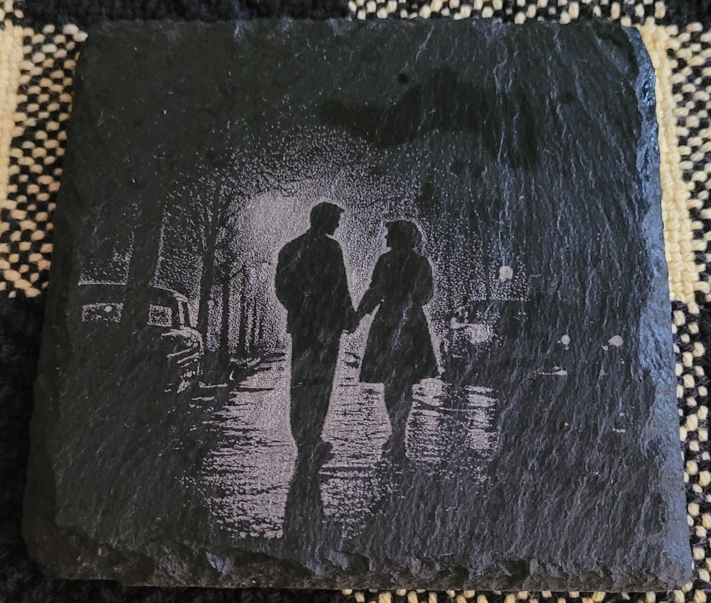 Engraved stone with a silhouette of two people walking on a street at night.