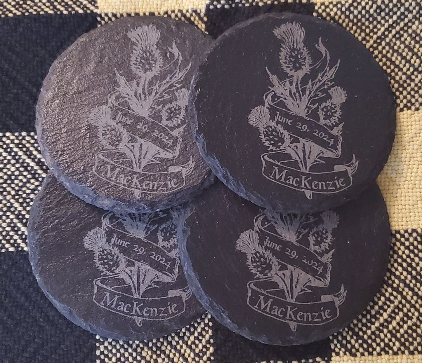 Four black slate coasters with engraved thistle design and 'MacKenzie' text
